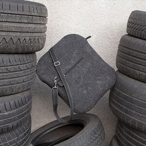 May include: A gray felt bag with a black leather strap, leaning against a stack of black tires.