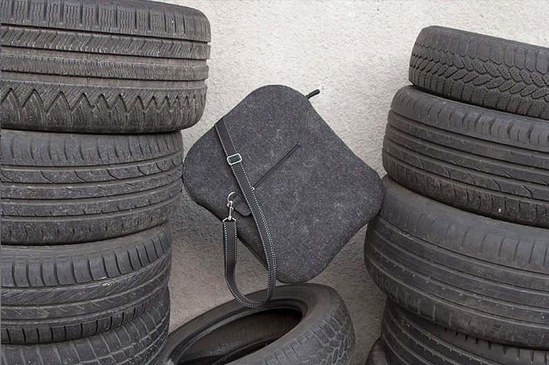May include: A gray felt bag with a black leather strap, leaning against a stack of black tires.