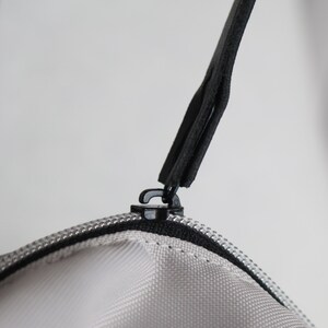 Puede incluir: Primer plano de un tirador de cremallera negro unido a una cremallera blanca en una bolsa gris.