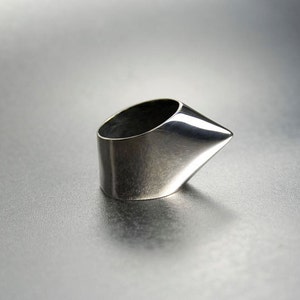 May include: A silver ring with a pointed, angular design. The ring is made of polished metal and has a smooth, reflective surface.