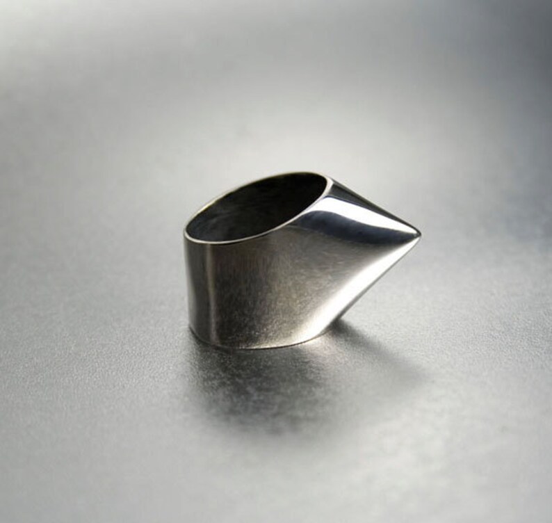May include: A silver ring with a pointed, angular design. The ring is made of polished metal and has a smooth, reflective surface.