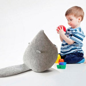 May include: A gray felt toy shaped like a whale with a long tail. A young child in a blue and white striped shirt and blue shorts is playing with a red ball. Colorful plastic cups and containers are scattered around.