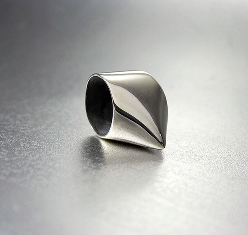 May include: A silver ring with a pointed, cone-shaped design. The ring is smooth and polished.