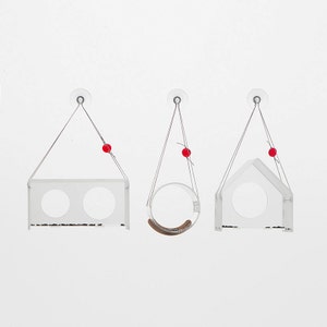 May include: Three clear acrylic bird feeders with suction cups, hanging from strings with red beads. Each feeder has a different shape: one is a rectangle with two circular openings, one is a circle, and one is a house shape.