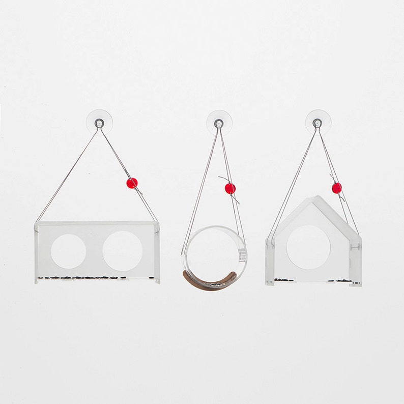 May include: Three clear acrylic bird feeders with suction cups, hanging from strings with red beads. Each feeder has a different shape: one is a rectangle with two circular openings, one is a circle, and one is a house shape.