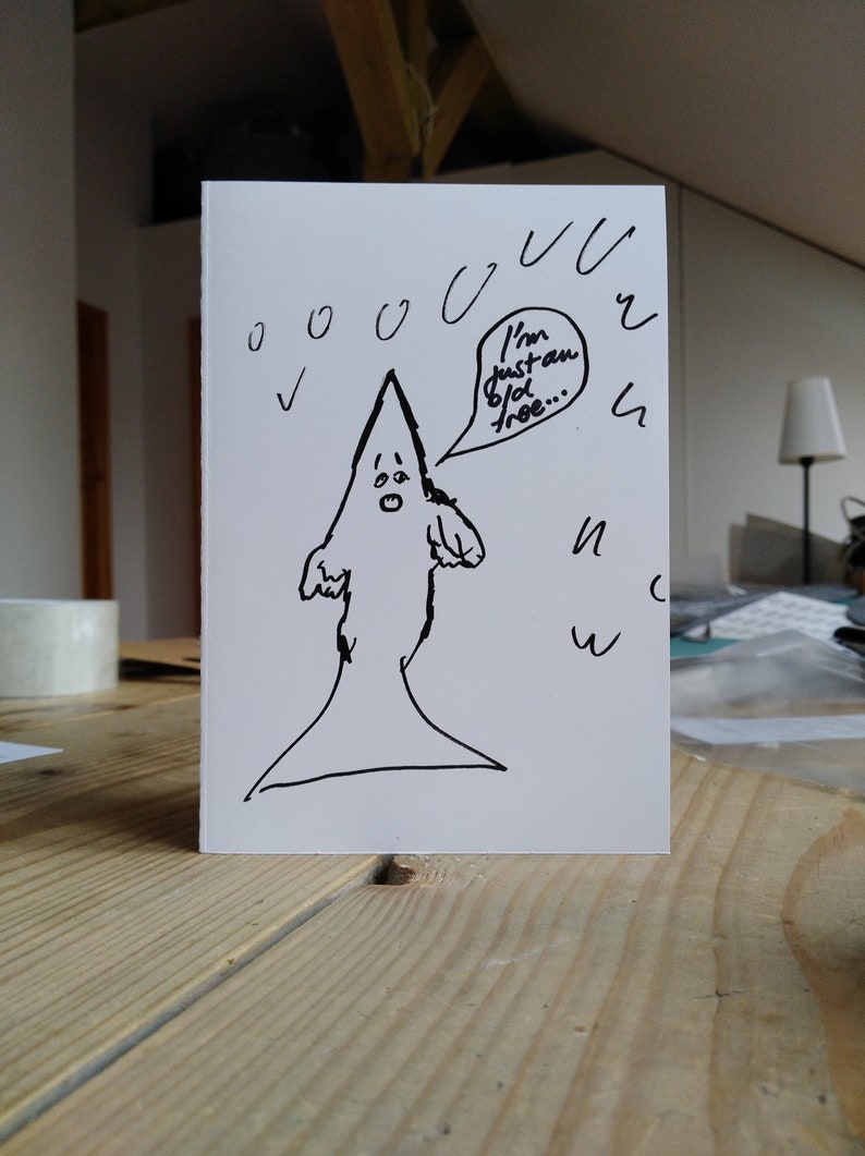 May include: A white greeting card with a hand-drawn cartoon figure in a pointed hood. The figure has a surprised expression and a speech bubble that says, "I'm just an old tree..." Black ink drawings of rain and other shapes surround the figure.