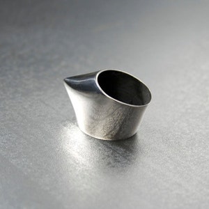 May include: A silver ring with a pointed, angled design. The ring is made of metal and has a smooth, polished finish.