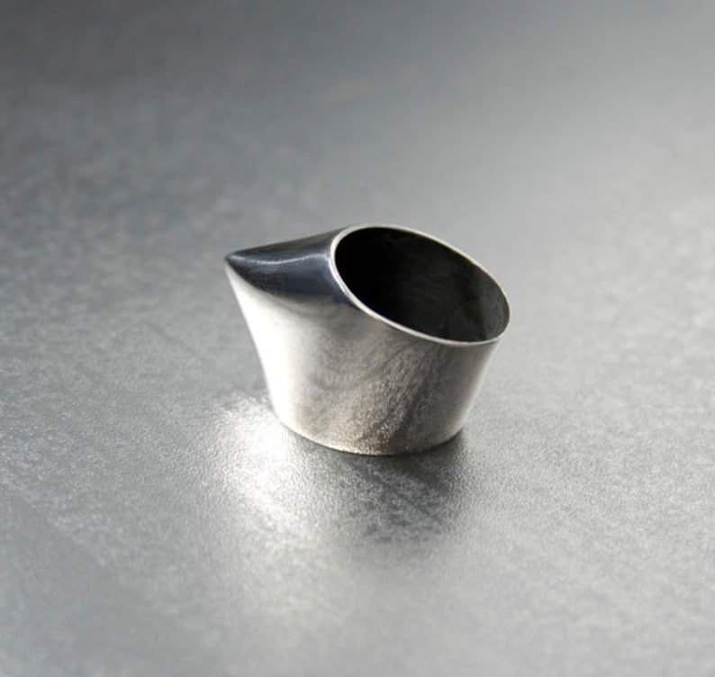 May include: A silver ring with a pointed, angled design. The ring is made of metal and has a smooth, polished finish.