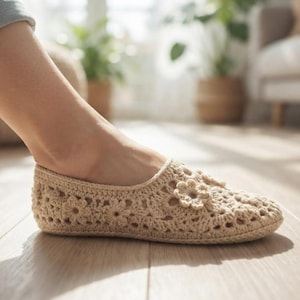 May include: A beige crochet slip-on shoe featuring an intricate floral pattern throughout the knit construction. The footwear has a low-profile design with a rounded toe and a textured, open-work surface created by interconnected yarn loops.