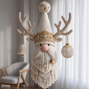 May include: A cream-colored macrame wall hanging shaped like a reindeer gnome with a tall pointed hat, a gold crown with pearls, and large antlers. A crocheted bell and a round ornament hang from the antlers, with a long fringed beard.
