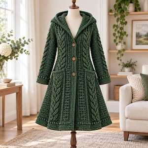 May include: A dark forest green crochet coat featuring a hood, long sleeves, and a flared skirt. The garment is detailed with vertical cable knit patterns, a textured bobble trim along the hem, and three round wooden buttons down the front.
