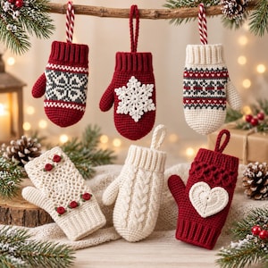 May include: Six crocheted mitten ornaments featuring festive designs. Three hang from a branch: one red with a grey snowflake pattern, one solid red with a white snowflake, and one cream with red and grey bands. Three sit below: one cream with red roses, one cream cable-knit, and one red with a white heart.