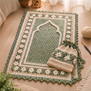 May include: A rectangular crochet prayer rug in sage green and cream featuring a central mihrab arch design and a border of floral motifs. A matching drawstring pouch with a similar floral pattern and cream-coloured base sits on the rug.