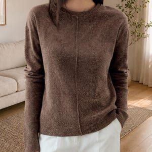 Può includere: Un maglione marrone a maniche lunghe caratterizzato da una trama a maglia a coste e una vistosa cucitura verticale che corre lungo il centro del davanti. Il capo presenta un classico girocollo e un orlo dritto dal look essenziale.