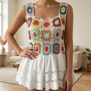 Peut inclure: Un haut sans manches avec une encolure carrée et un corsage composé de carrés de crochet multicolores dans des tons de rouge, bleu, jaune, vert et orange. La partie inférieure est une jupe en tissu blanc avec des détails en dentelle ajourée.