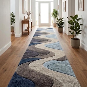 May include: A long runner rug featuring a wavy, abstract pattern in shades of navy blue, light blue, grey, and cream. The rug has a textured, high-pile surface with carved sections that emphasize the flowing, curved lines across the entire length.