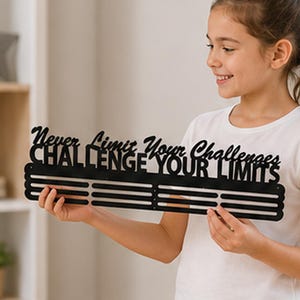 May include: A black metal medal hanger featuring the cut-out text "Never Limit Your Challenges" on the top line and "CHALLENGE YOUR LIMITS" on the second line, with three horizontal bars below for hanging medals or ribbons.
