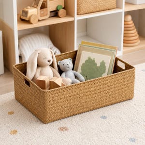 May include: A rectangular woven storage basket in a natural tan color with cutout handles. Inside the basket are a beige plush rabbit, a gray plush bear, two small wooden blocks, and several books with a green tree illustration on the cover.