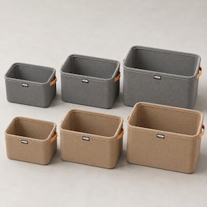 May include: A set of six rectangular storage bins arranged in two rows. The top row features three grey bins, and the bottom row features three tan bins. Each bin has light brown side handles, white stitching, and a small black label reading Fashion.