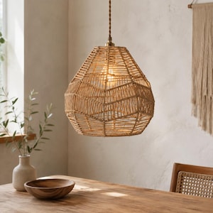 Może przedstawiać: Lampa wisząca z kloszem z plecionego sznurka w kolorze opalenizny z geometrycznym wzorem. Klosz zawieszony jest na skręconym brązowym przewodzie i zawiera widoczną żarówkę. Konstrukcja jest otwarta, co pozwala na przenikanie światła.