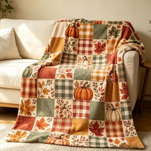 May include: A patchwork throw blanket featuring a repeating grid pattern of autumn-themed squares. The design includes illustrations of orange pumpkins, red and yellow maple leaves, and various plaid and gingham checks in shades of green, orange, and white.