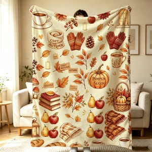 May include: A cream-colored throw blanket featuring a repeating autumn-themed pattern of orange and brown pumpkins, red apples, yellow pears, brown books, pinecones, knit mittens, plaid scarves, candles, and mugs with the text Pumpkin Season.