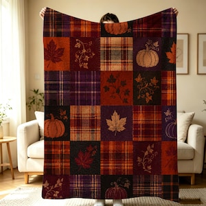 K&ouml;nnte beinhalten: Eine rechteckige Wohndecke mit einem Patchwork-Design aus herbstlichen Quadraten. Das Muster wechselt zwischen karierten Bl&ouml;cken in Orange-, Lila- und Braunt&ouml;nen sowie einfarbigen Bl&ouml;cken, die mit Illustrationen von K&uuml;rbissen und Ahornbl&auml;ttern verziert sind.