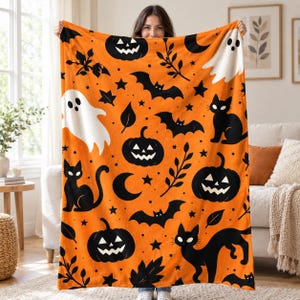 May include: A bright orange fleece blanket featuring a repeating pattern of black jack-o'-lanterns, black cats, black bats, white ghosts, crescent moons, stars, and dark leaf sprigs printed across the entire surface of the fabric.