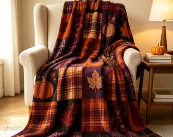 May include: A soft throw blanket featuring a patchwork design of autumn-themed squares. The pattern alternates between plaid sections in shades of orange, deep purple, and brown, and panels decorated with orange pumpkins and brown maple leaves.