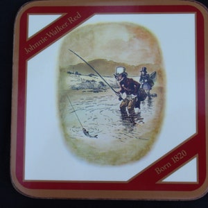 May include: A red and gold square coaster with a white center featuring a vintage illustration of two men fishing in a river. The text "Johnnie Walker Red" and "Born 1820" are printed on the coaster.