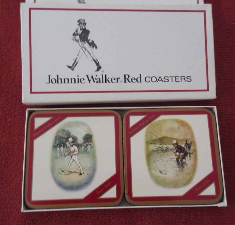 May include: A set of four Johnnie Walker Red coasters featuring illustrations of a man playing golf and a man fishing. Each coaster has the text "Johnnie Walker Red" and "Born 1820" printed on it.
