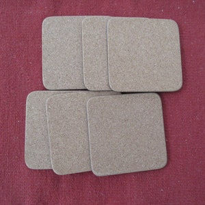 May include: Six brown cork coasters, stacked in two rows of three, on a red fabric surface.