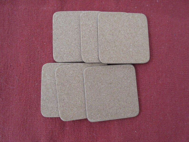 May include: Six brown cork coasters, stacked in two rows of three, on a red fabric surface.