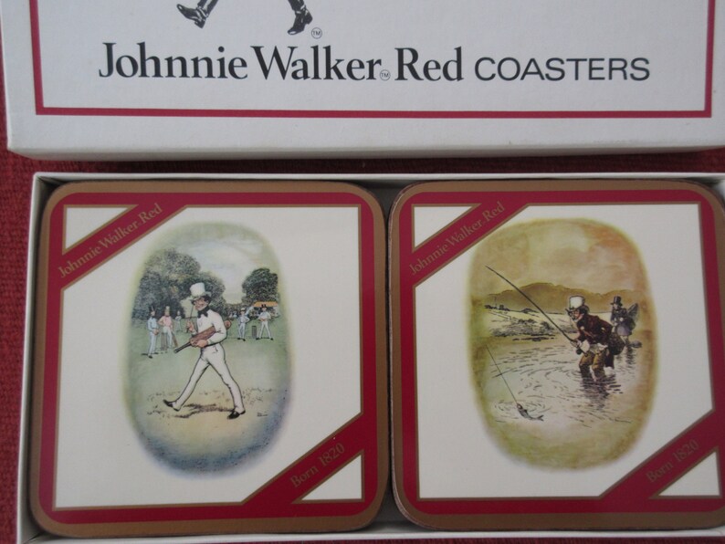 May include: Two square Johnnie Walker Red coasters with red borders. The coasters feature illustrations of a man playing cricket and a man fishing. Both coasters have the text "Born 1820" printed on them.