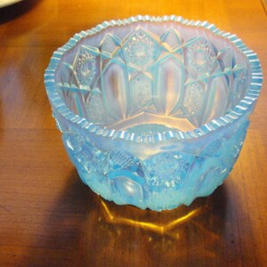 May include: A light blue glass bowl with a cut glass design. The bowl has a scalloped edge and is sitting on a wooden surface.