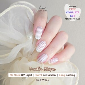 Op de afbeelding: Nagelwraps met een verticaal wit en lichtbeige gestreept patroon aangebracht op de vingernagels. De tekst op de afbeelding bevat "Blooming Acacia", "Vanilla Stripes", "No Need UV Light", "Can't be Harden", "Long Lasting" en "Get Full Free Complete Set For Each Purchase".