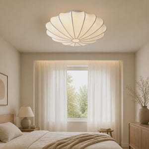 May include: A white, circular, scalloped flush mount ceiling light fitting with a ribbed, petal-like design. The light is mounted centrally on a flat ceiling, emitting a soft, diffused glow that illuminates the room from above.