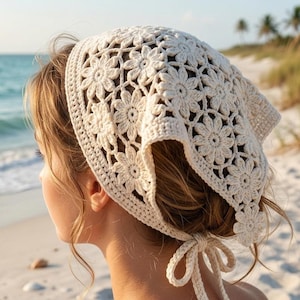 May include: An off-white crochet headscarf featuring a repeating floral pattern made of interconnected daisy motifs. The triangular head covering is secured at the back of the head with two thin crocheted ties that form a bow, creating a textured look.