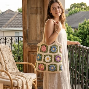 May include: A crochet tote bag featuring a pattern of multi-colored floral granny squares in shades of pink, blue, white, and purple, set against a cream-colored background with two integrated shoulder straps for carrying.