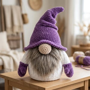 May include: A handcrafted crochet gnome featuring a tall, pointed purple hat, a round beige nose, and a long, shaggy gray beard. The gnome has a white body and wears matching purple crochet mittens on its sides, creating a soft, textured appearance.