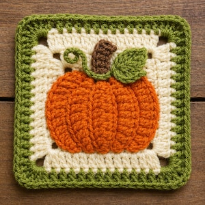Pode incluir: Um quadrado de crochê tipo granny square com um motivo central de abóbora laranja, com um caule castanho, uma folha verde e uma gavinhas verde encaracolada. A abóbora está centrada num fundo creme, emoldurada por uma borda espessa de lã verde-escura.