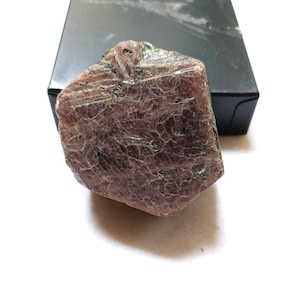 Puede incluir: Un espécimen mineral en bruto y sin pulir de forma hexagonal y color marrón rojizo intenso. La superficie muestra una red compleja de finas grietas entrecruzadas y texturas cristalinas con inclusiones oscuras incrustadas en la piedra.