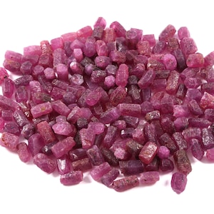 Peut inclure: Une grande collection de petits cristaux de rubis bruts et non polis dans diverses nuances de rose profond et de magenta. Ces pierres naturelles présentent des formes irrégulières, allongées et bloc avec une surface mate et texturée.