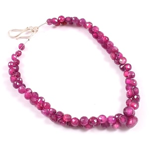 Può includere: Un braccialetto composto da numerose piccole perle di pietre preziose sfaccettate di colore rosa intenso. Il pezzo presenta un meccanismo di chiusura a gancio in metallo color argento a un'estremità, che fissa la disposizione circolare delle perle.