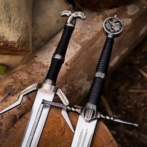 May include: Two metal swords with black grips and silver-toned crossguards. One sword features a wolf-shaped pommel, while the other has a circular pommel with a wolf emblem. The blades are metallic silver with visible engraved inscriptions.