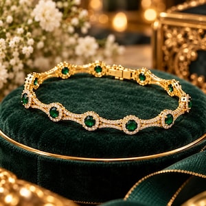 Può includere: Un bracciale color oro caratterizzato da una serie di pietre rotonde verde scuro, ciascuna circondata da un alone di piccole pietre bianche trasparenti. Le maglie sono collegate da una delicata struttura in metallo dorato e include una chiusura.