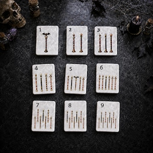 May include: Nine white rectangular tiles arranged in a grid, each featuring a different number of vertical wand-like sticks. The sticks are metallic with varied toppers including bats, stars, and skulls, numbered one through nine for identification.