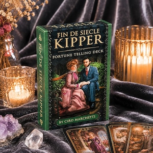 May include: A rectangular deck of Fin de Siecle Kipper fortune telling cards by Ciro Marchetti. The box features a dark green border and an illustration of a person in a pink dress and a person in a blue suit sitting on a bench. The text reads Fin de Siecle Kipper Fortune Telling Deck.