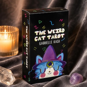 May include: A black rectangular tarot deck box titled The Weird Cat Tarot by Gabrielle Kash. The box features a colorful illustration of a cat wearing a purple witch hat with a star emblem, surrounded by small neon geometric shapes on a black background.