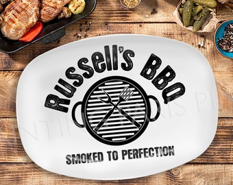 May include: White oval serving platter with black text that reads "Russell's BBQ Smoked to Perfection". The platter features a black and white illustration of a grill with crossed tongs.